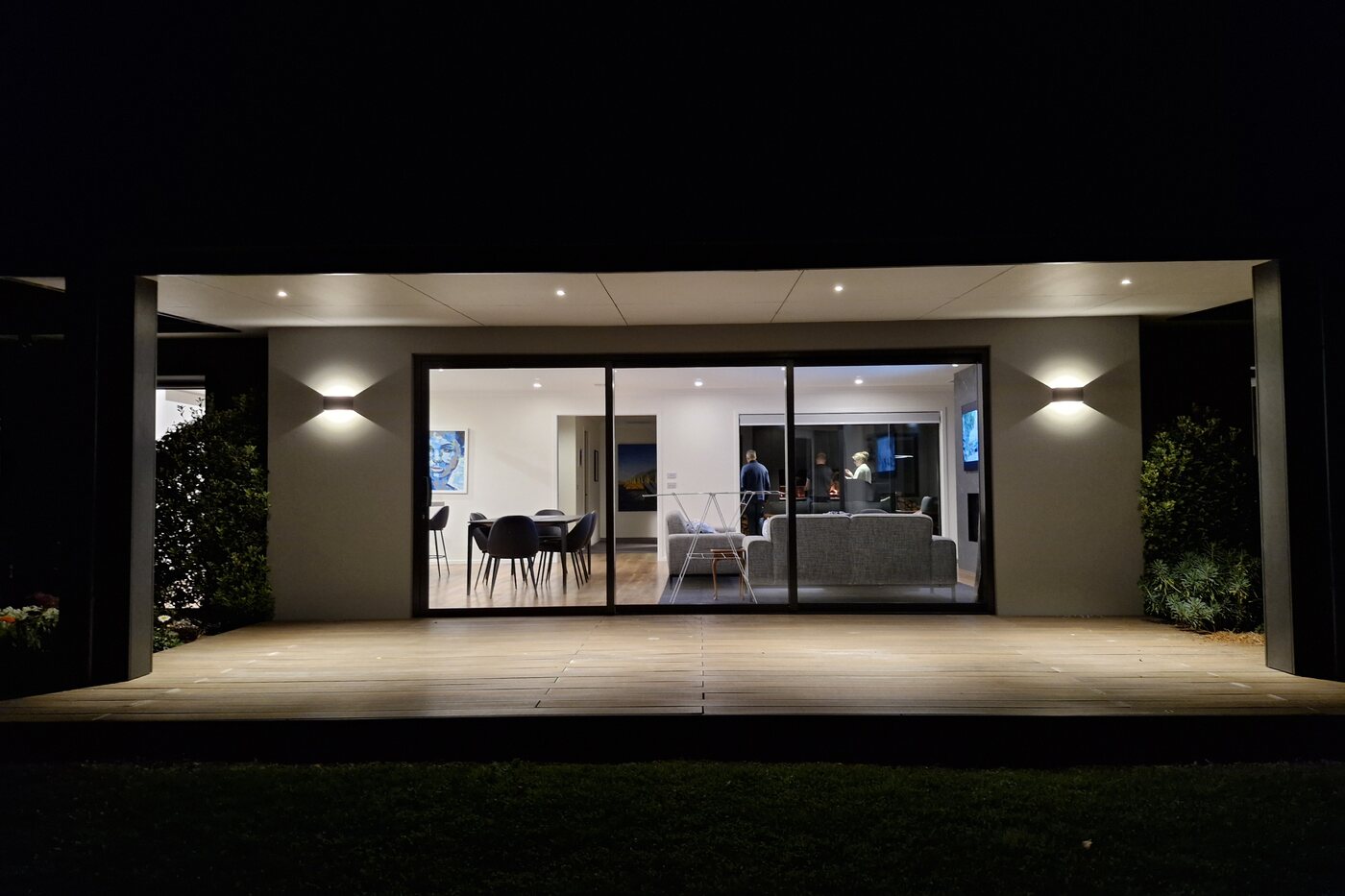 The same home at night, exterior wall lighting and interior downlights running together